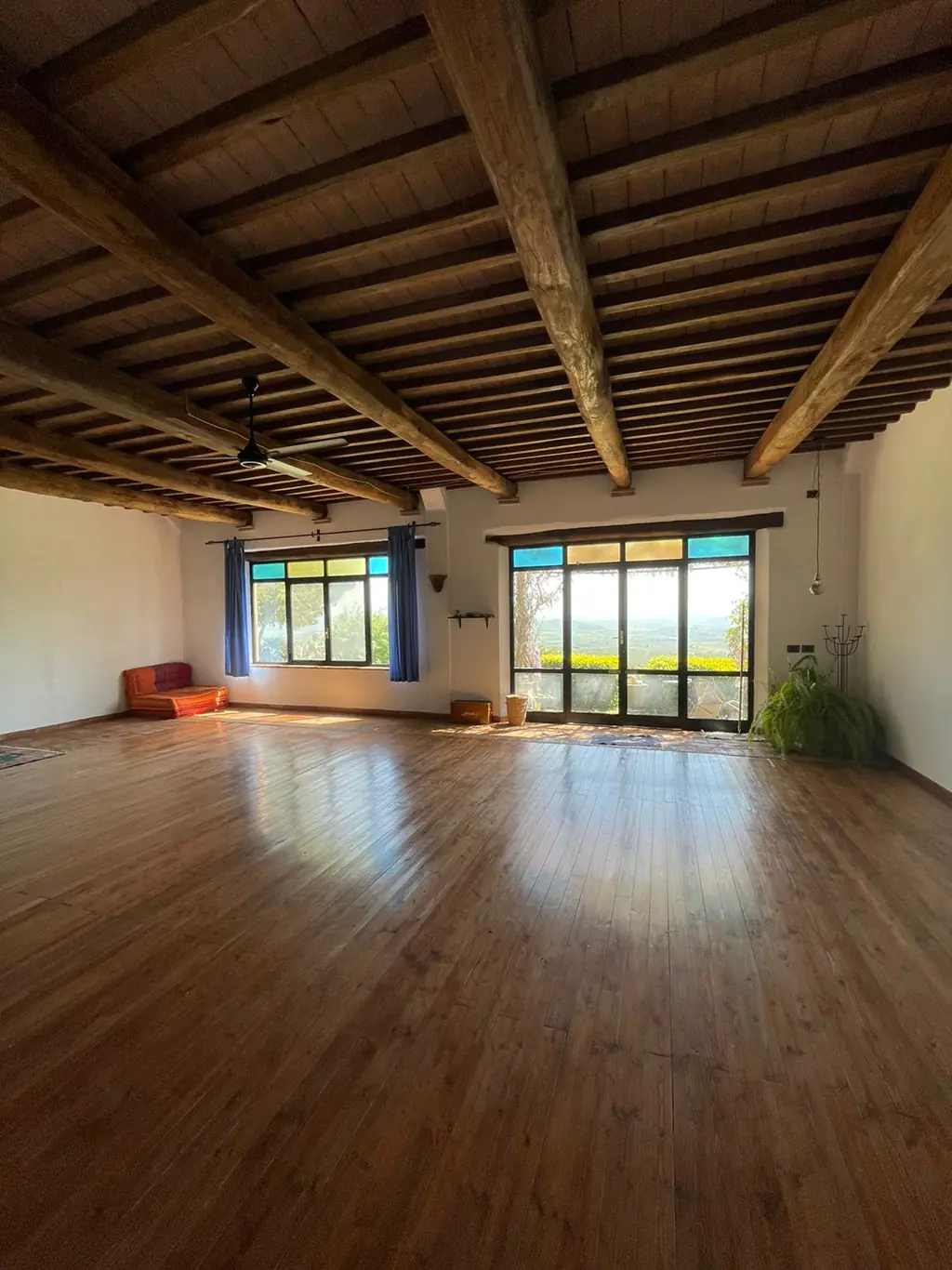 La sala: un ampio pavimento in legno sotto le travi a vista, finestre sulle colline